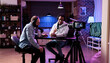 © DC Studio - Online vlogger filming podcast episode with man in studio, using camera and soung production equipment to record. Content creator broadcasting live conversation on social media.