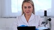 © Евгения Медведева - Woman scientist research chemist in a medical suit and protective gloves with a tablet computer and a microscope conducts research in the laboratory.