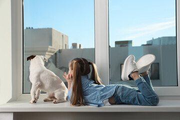 Wall Mural - Cute little girl with her dog on window sill indoors. Childhood pet