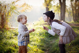 Fototapeta Dmuchawce - Dzieci dmuchają dmuchawce w parku przy letnim słoneczku