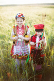 Fototapeta  - Dzieci w tradycyjnych polskich krakowskich strojach spacerują po polu obsianym zbożem w ciepłych letnich promieniach słonca