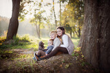 Fototapeta Dmuchawce - Dzieci przytulają misia i siedzą pod drzewem w parku