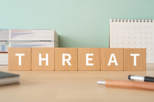 脅し・脅迫のイメージ｜「THREAT」と書かれた積み木が置かれたデスク
