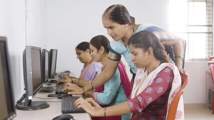 smiling teacher and student looking at camera while teaching computer class to woman's at village - concept of volunteer, self employment training and empowerment programs