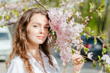 girl in a white shirt stands near the sakura in sunny spring weather