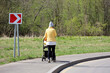 Woman in yellow jacket walking with baby pram on sidewalk and talking on a mobile phone. Young mother in city park at spring near the road sign of right turn