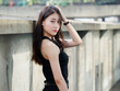 Graceful young woman with long black hair in sundress posing in sunny day. Outdoor photo of cool Chinese girl in trendy summer sexy black dress.
