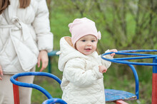 Smiling Baby Toddler Rides Carousel In Playground Outside. Concept Of Kindergarten And Childhood.