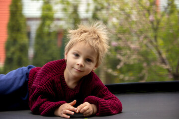 Cute little boy with static electricy hair, having his funny portrait taken outdoors on  trampoline