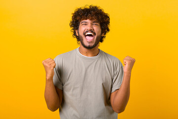 overjoyed crazy happy indian curly guy screaming yes in ecstatic, raising fists up, celebrating good