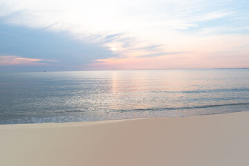 Sticker - Colorful light pastel sky reflects onto ocean and sand in the early morning at the shore.