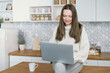 © yurolaitsalbert - young woman using laptop sitting on kitchen table .