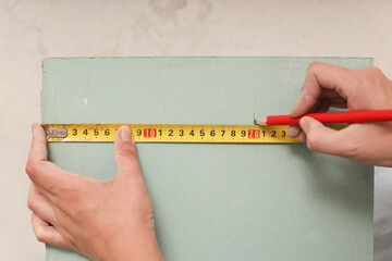 A woman with a meter in her hands, measuring dimensions on a drywall panel - the concept of home improvement with her own hands