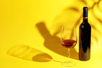 Glass and bottle of red wine on a yellow background.