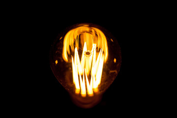 Edison lamp on a black background. Incandescent lightbulb with a dark background. Tungsten lamp it's make feeling to warm tone. Retro Edison light bulb with an unusual spiral.