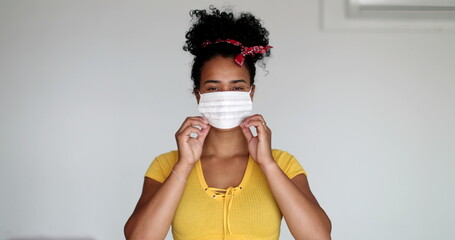 Wall Mural - Young African descent woman putting face mask virus prevention, girl crossing arms looking at camera