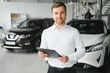 © Serhii - portrait of open-minded professional salesman in cars showroom, caucasian man in white formal shirt stands next to luxurious car and looks at camera