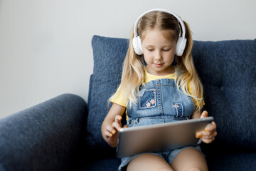 Wall Mural - cute little girl at home with headphones and using tablet