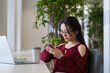 © DimaBerlin - Young asian student girl procrastinate in library using smartphone and chatting in social media while preparing for exam test. Lazy woman with mobile phone in hand avoid learning and doing homework