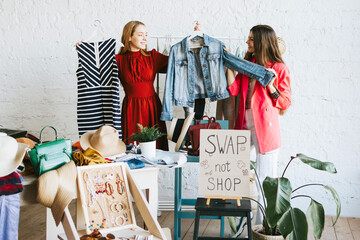 two young woman female caucasian students at swap party try on clothes, bags, shoes and accessories, change clothes with each other, second hand for things, zero waste life, eco-friendly