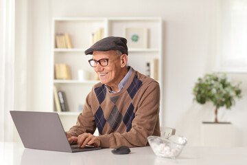 Poster - Happy elderly man sitting at home on a sofa with a laptop computer