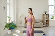© Studio Romantic - Lifestyle portrait of beautiful slender young fitness woman holding glass of water standing in living room. Girl drinks water after morning workout at home. Concept of good habits and sports.