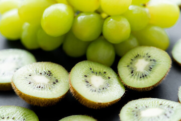 Wall Mural - close up view of green grapes and sliced fresh kiwi on black.