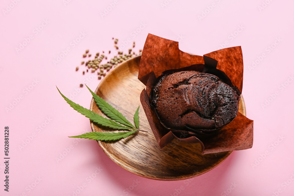 Wooden plate with chocolate cannabis muffin on pink background