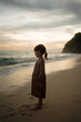 © Yevhenii - Rear view little girl stand on seashore during sunset and look at beatuful sky and ocean waves
