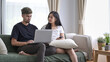 © Prathankarnpap - Happy young couple relaxing on couch in living room and using laptop together.