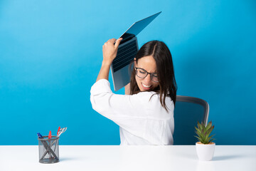 Wall Mural - Angry hispanic pretty woman throwing laptop isolated on blue background. Office worker with anxiety