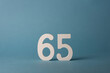 White wooden number sixty-five 65 on blue background.