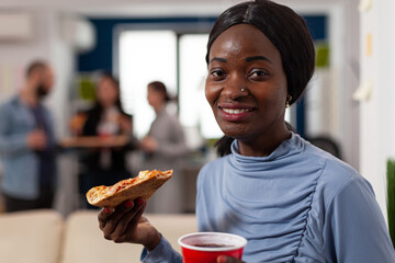 Wall Mural - Portrait of african american woman holding pizza and beer, enjoying after work drinks party with office coworkers. Cheerful person having fun at celebration after hours with alcohol and snacks.