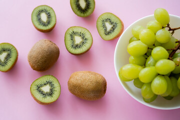 Wall Mural - top view of grapes in bowl near kiwi on pink.