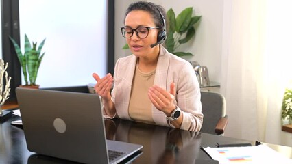 Wall Mural - Smiling female call center employee using a headset and laptop for online communication with customers, woman in smart casual wear talking online