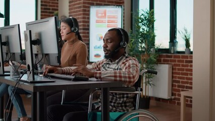 Wall Mural - African american man in wheelchair answering helpline call at customer service job, working in disability friendly office. Male worker using telework headset at helpdesk to help clients.