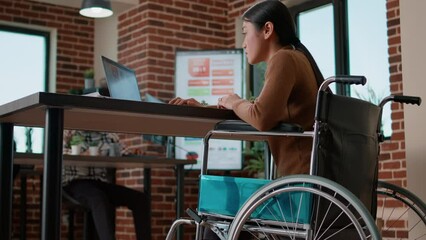 Wall Mural - Asian woman analyzing financial charts on laptop computer, dealing with chronic disability. Office worker looking at graphs on device screen, planning marketing and leadership strategy.