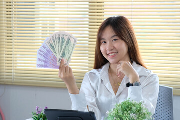 Wall Mural - Businesswoman holding a stack of money inside her office at work