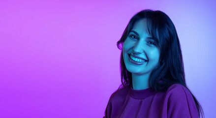 Portrait of young charming girl, student smiling isolated over purple studio background in neon light. Concept of emotions, facial expression, art, beauty