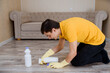 © Med Photo Studio - man in a yellow t-shirt and yellow gloves is cleaning the wood flooring  using cleaning spray and sponge.