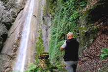 Male Photographer Photographing Waterfall Giessbach In Alpine Mountains, Fast Flowing Powerful Stream Of Clear Water, Splashes Scatter, Concept Of Wild Nature, Natural Resources, Alternative Energy