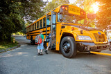 Fototapeta Miasta - A young boy getting onto a school bus in sunshine