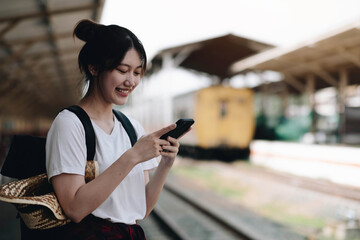 Woman waiting on station platform on background light train using smart phone. Tourist texting message and plan route of stop railway, railroad transport, booked. Enjoying travel concept