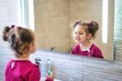 © TenWit - Young cute female kid looking at her reflection in the bathroom mirror while brushing her teeth