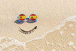 © Nikita - A painted smile on the beach and sunglasses with the flag of Spain. The concept of a positive holiday in the resort of Spain.