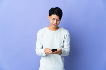 Wall Mural - Young Chinese man isolated on purple background sending a message with the mobile