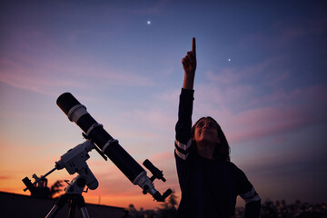 Wall Mural - girl with astronomical telescope stargazing under twilight sky.