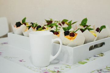 Wall Mural - Homemade cupcakes for a party. Fresh cupcakes garnished with whipped cream, berries and mint leaves on a wooden tray. There is a white cup next to it. Food background.