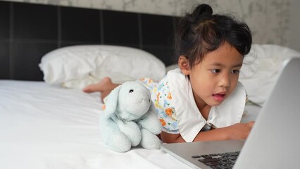 Wall Mural - Girl lying in bed with dog doll watching laptop.