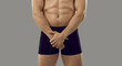 Man holding hands on his intimate area. Banner with cropped shot of young guy in underpants covering his crotch standing isolated on solid grey background. Impotence, problems with erection concept